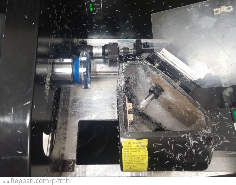 The lens is "CHUCKED" using the block we mounted to the lens to keep everything in place and on axis while the machine cuts.  The box on the right has 4 diamond tipped blades that rotate extremely fast. (idk the exact rpms)  There is also a vacuum underneath it that catches the extra poly carbonate( lens material) shavings. Also known as swarf.